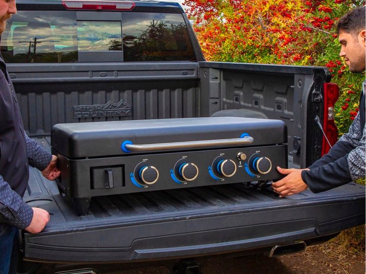 Two guys unload a Pit Boss Ultimate grill out of the back of a pickup truck.