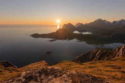 Mitternachtssonne hinter der bergigen Landschaft und dem Meer auf den Lofoten in Norwegen