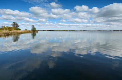 Wolken spiegeln sich in dem ruhigen Wasser des Großen Meeres im Südbrookmerland in Ostfriesland.