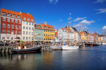 Blick vom Wasser auf die bunten Häuser von Nyhavn in Kopenhagen, vor denen Boote verankert sind