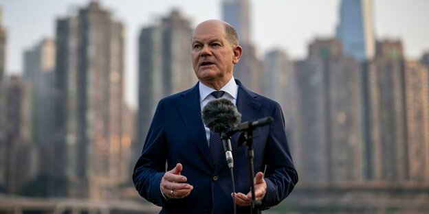 Kanzler Olaf Scholz am Sonntag in China. Im Hintergrund Hochhäuser. Scholz trägt Anzug.