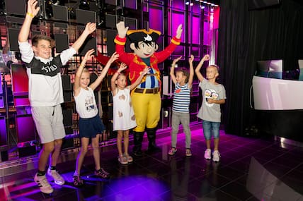 Fünf Kinder tanzen auf einer Bühne auf der Mein Schiff 2 mit dem Maskottchen Capt'n Sharky.