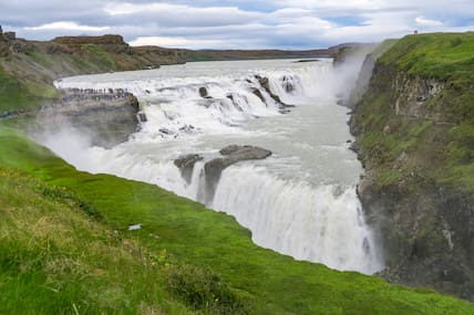 Mächtiger und weiß schäumender Gullfoss-Wasserfall auf Island, umgeben von grünen Klippen