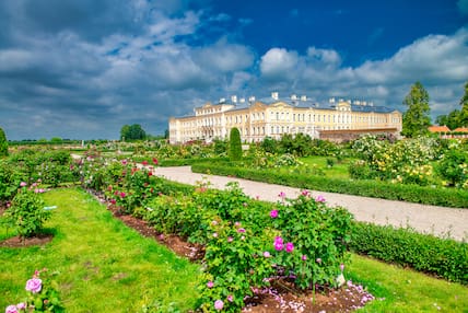 Blick auf den gelben Rundale Palast in Lettland, umgeben von einer grünen Parkanlage mit bunten Blumen, die von der Sonne beschienen wird