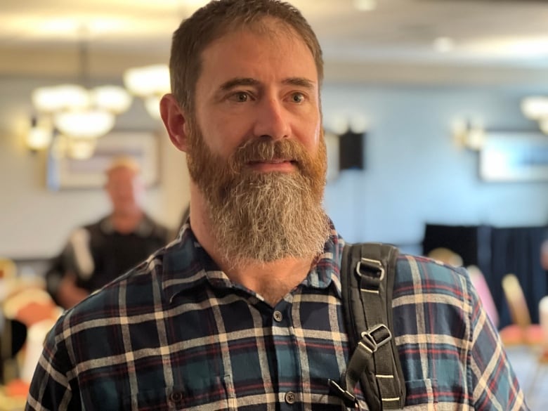 A man with a beard wears a plaid shirt.