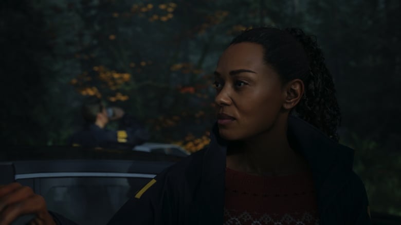 Video game screenshot of a Black adult woman wearing an FBI jacket, standing in a dark forest.