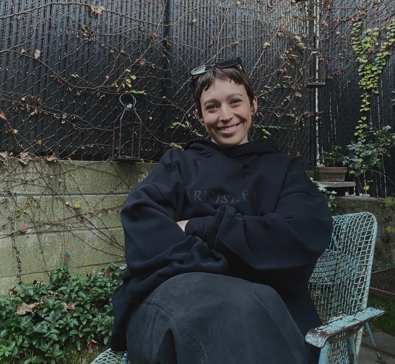 Photo of a woman with short brown hair sitting on a chair in an outdoor patio.