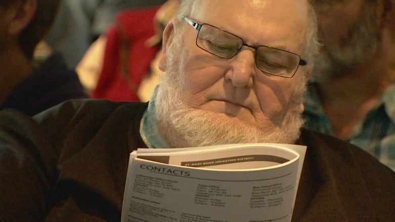 A man with a beard and glasses reads a pamphlet.