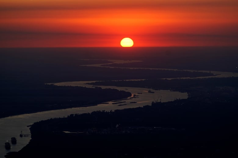 The sun sets on the Mississippi River in Louisiana. Boats can be seen heading down the river. 