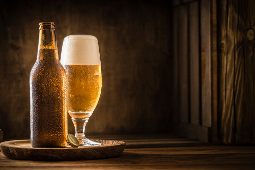 Beer bottle with a drinking glass full of beer on a rustic wooden table