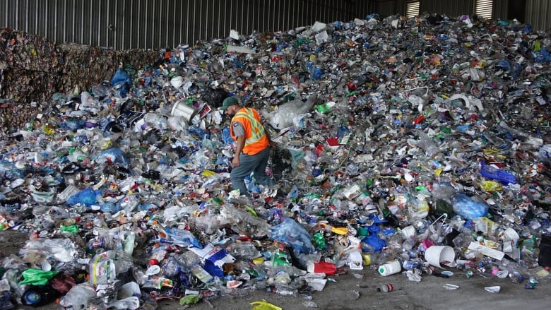 A worker in a reflective vest steps in a large pile of material for recycling. 