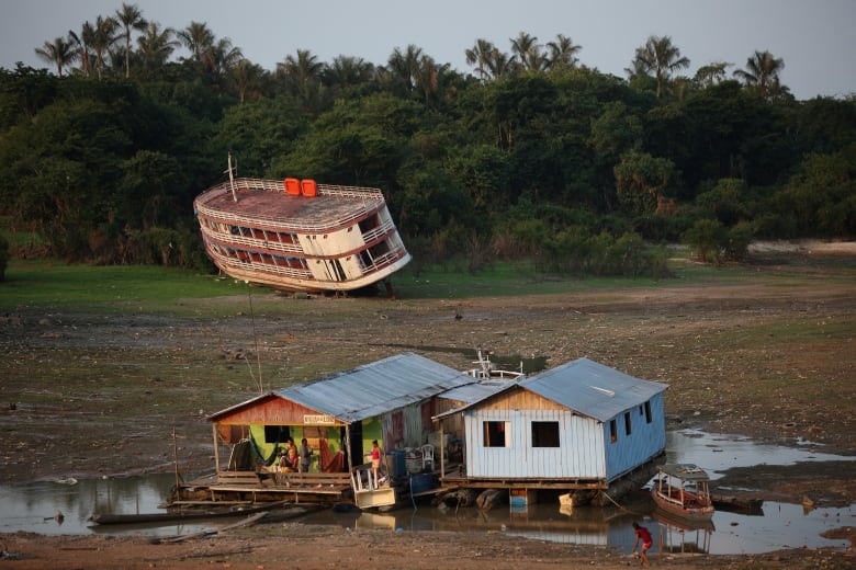 Houses in the foreground and a large boat in the background, sit on a dry riverbed. 