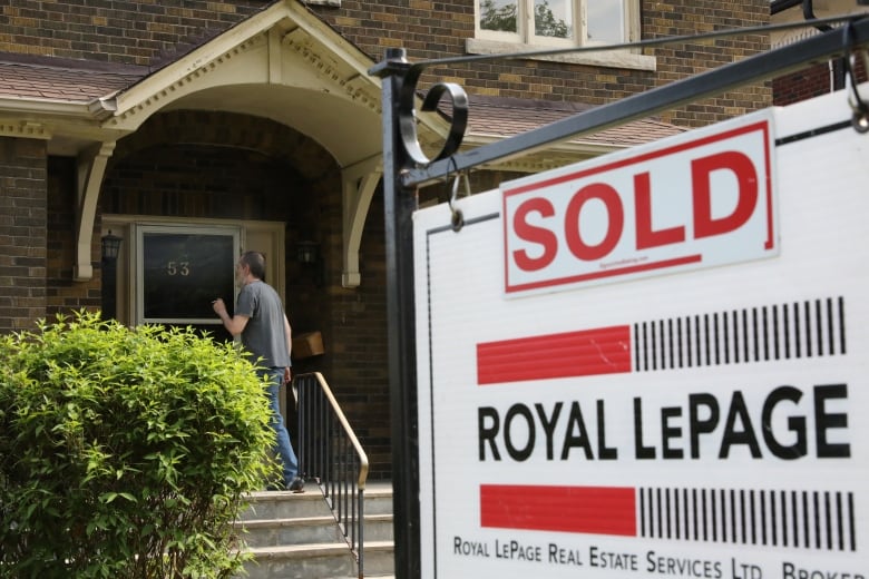 A man knocks on a door while a sold sign hands outside.