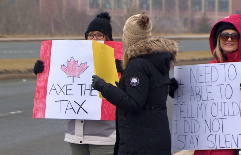 People hold signs reading "axe the tax" and “I need to be able to tell my children I did not stay silent.”