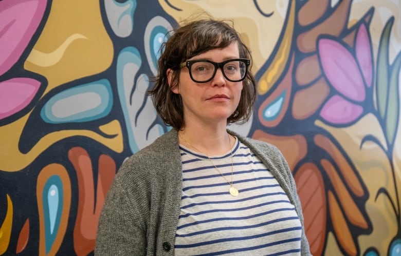 A person stands in front of a multi-coloured wall mural.