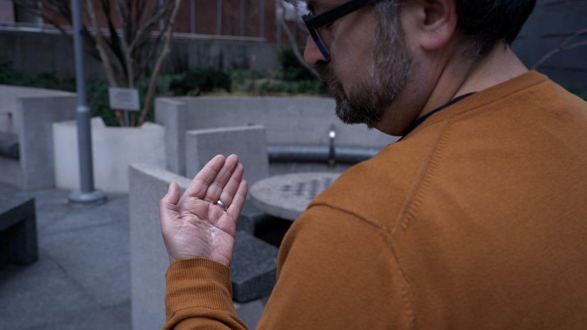 A man standing and trying to look at a faint display projected on his hand