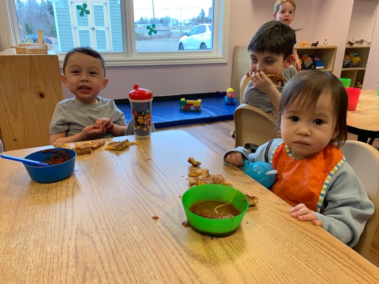 Three children eating supper at a small table in a daycare.