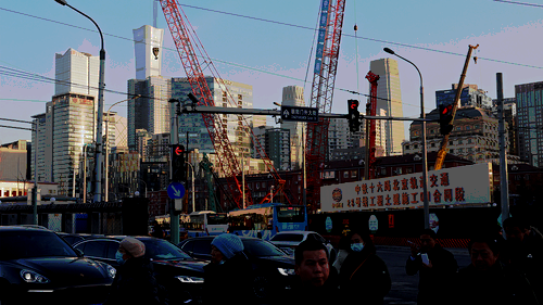 People cross an intersection near cranes standing at a construction site in Beijing.