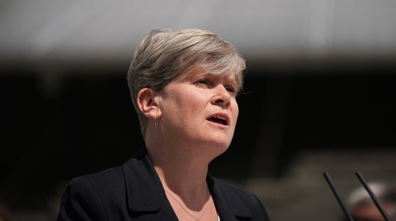 A white woman with short hair speaks at an outdoor event.