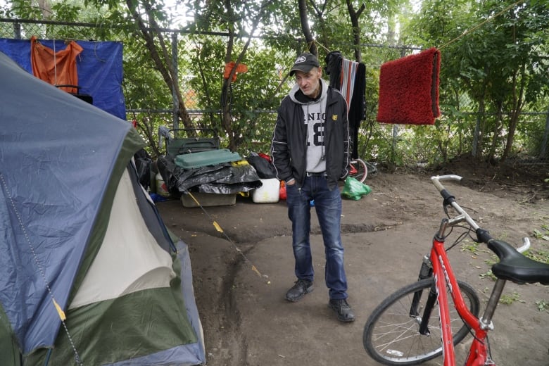 A man stands next to a tent with a clothesline and a bike