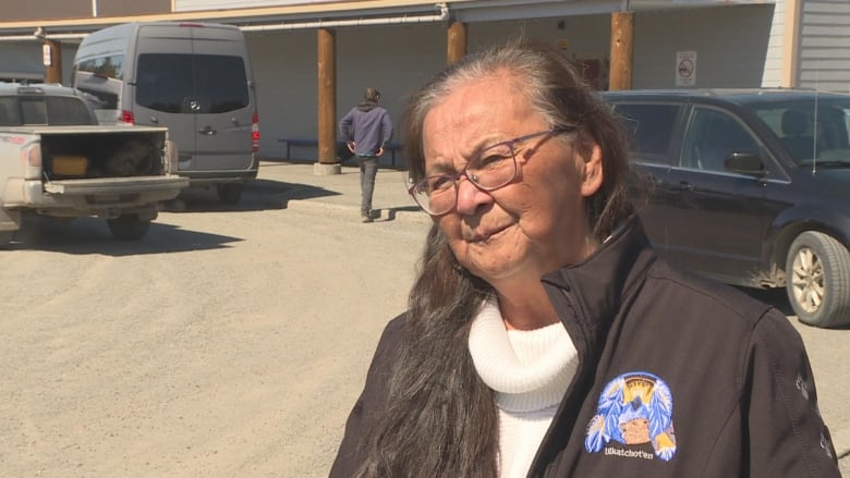 An older woman smiles in a parking lot.