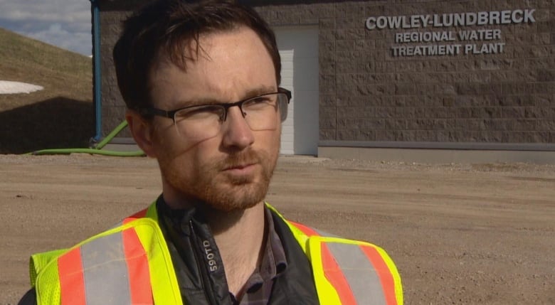 A man wearing a vest stands and looks at the camera.