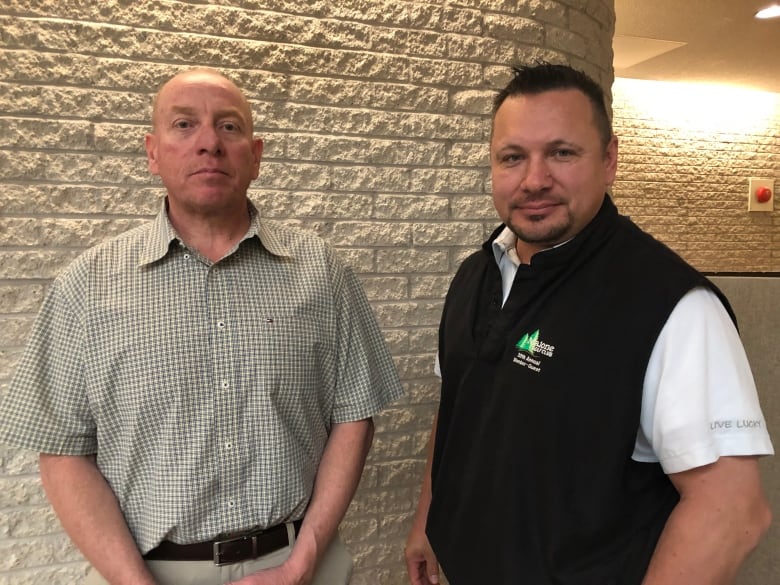 Two men stand in front of a wall in a courthouse.