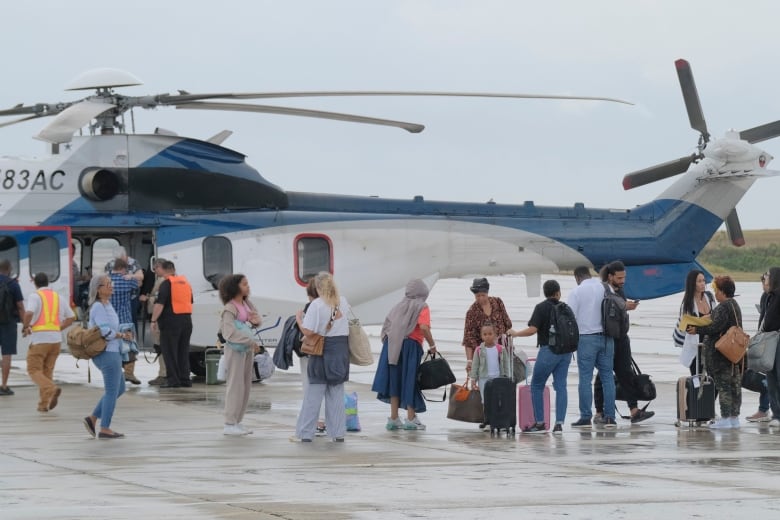 People with luggage stand outside a helicopter at an airport.