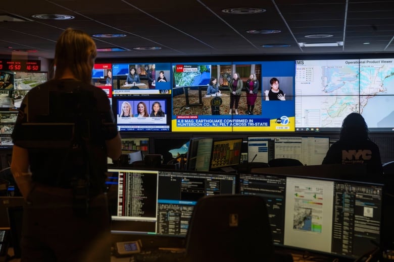 People are seen inside a command centre room filled with TV and computer screens.