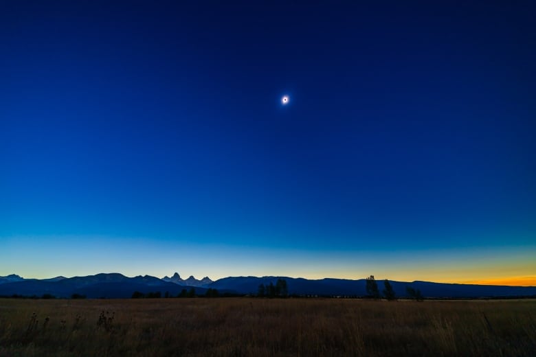 A shining celestial body in the deep blue sky high above a mountain range. 