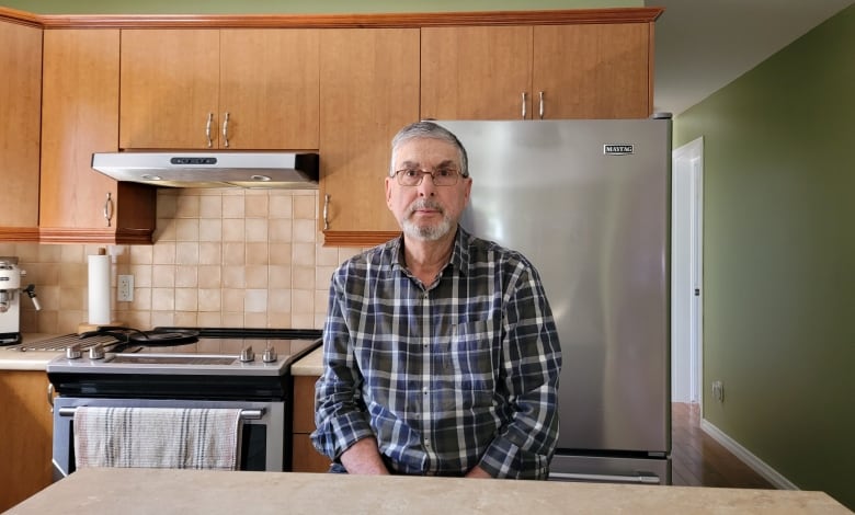 A man in a checkered shirt sits in a kitchen.