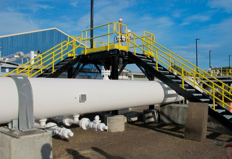 A set of stairs with yellow guard railings rises up and over a large grey pipeline.