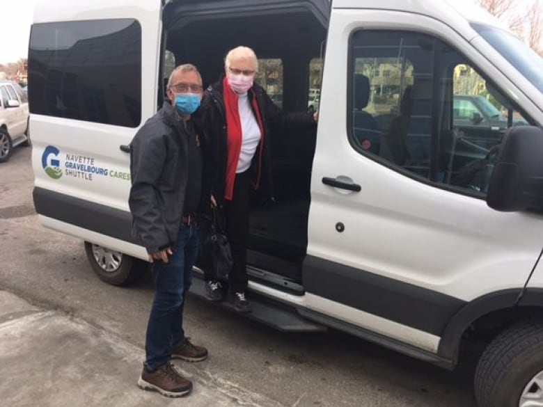 A man helps a senior woman out of a white shuttle van. 