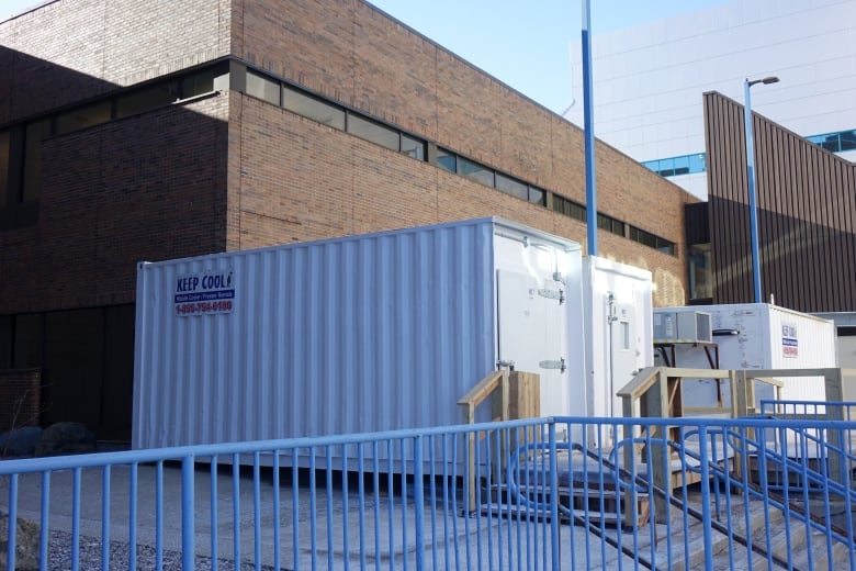 Three white storage containers sit in front of a brown brick building. 