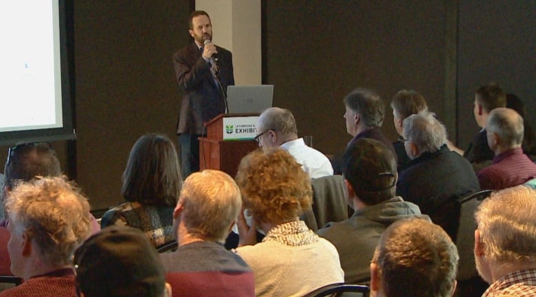 A man speaks into a microphone in front of a seated crowd.