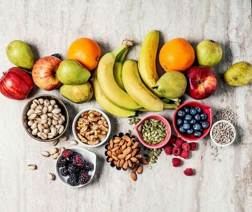 piles of artfully arranged fruits and nuts, including peanuts, pistachios, apples, bananas, pears and blueberries