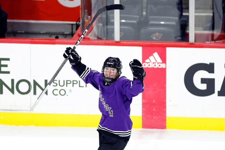 A female hockey player wearing purple uniform is seen celebrating a goal. 