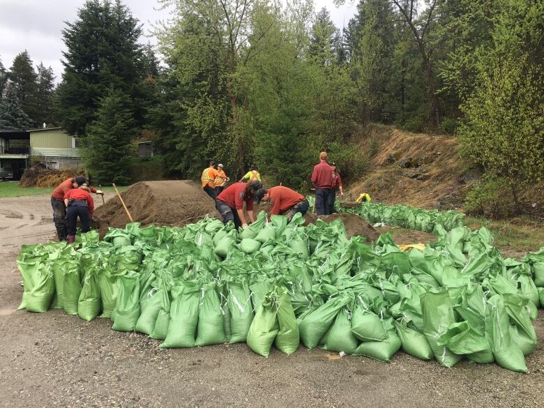 Five people pack green bags full of sand.