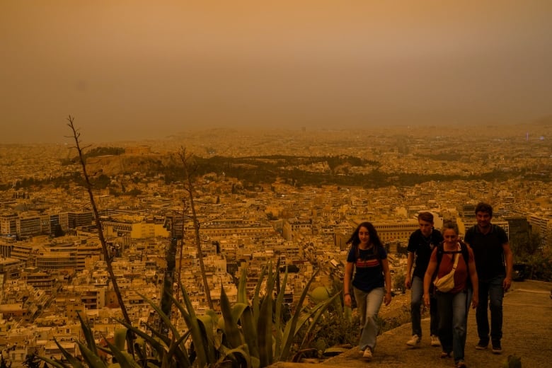 A group of young people walk up a hill over a cityscape, with an orange haze in the sky