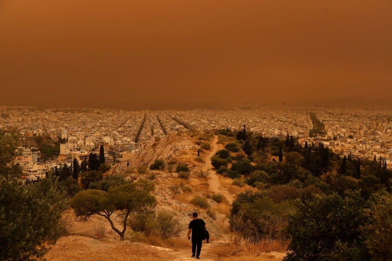 A man walks down a hill over a cityscape with an  orange sky