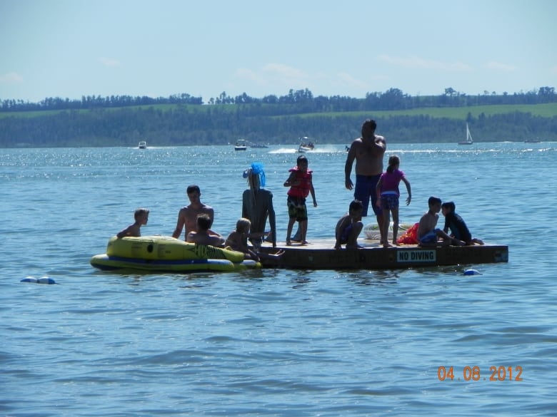 Two adults and eight children in their swimming suits on a board in the middle of a lake. 