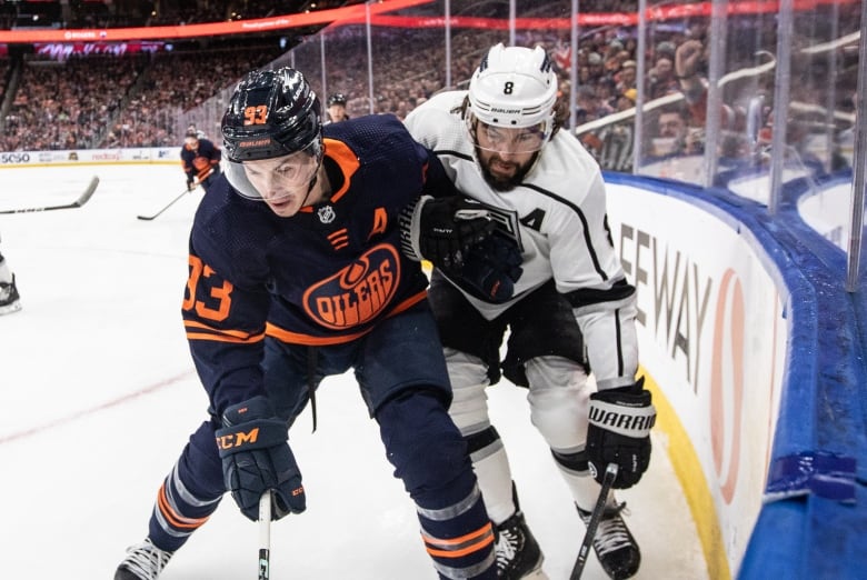 Two hockey players battling for the puck by the glass.