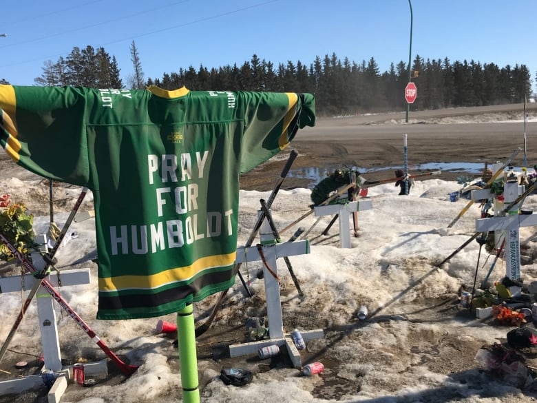 A 'pray for Humboldt' jersey is draped at the site that also fetures crosses, hockey sticks and other tributes.