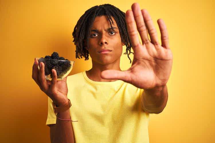 Afro american with dreadlocks holding blackberries over isolated yellow background with open hand doing stop sign with serious and confident expression, defense gesture