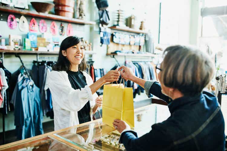 Shop owner handing bag to smiling client after shopping in clothing boutique