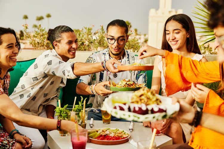 Medium shot of smiling friends sharing food at rooftop restaurant