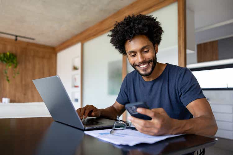 Happy entrepreneur working at home using his laptop and his cell phone