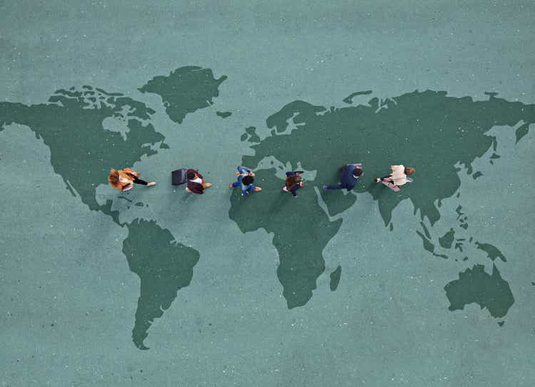 Businesspeople walking in line across world map, painted on asphalt