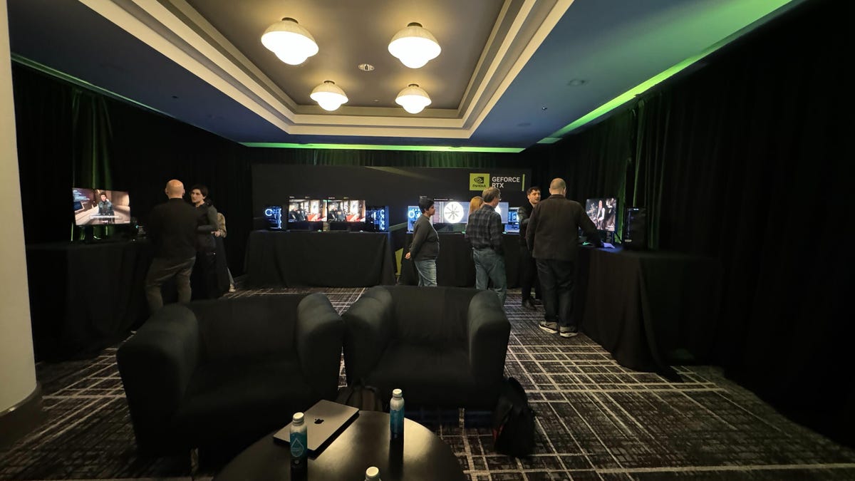 A small hotel meeting room is lined with black tablecloth-covered tables supporting monitors and PC desktops showing various demos.