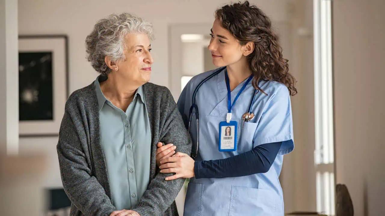 Senior woman with walking stick being helped by nurse at home.